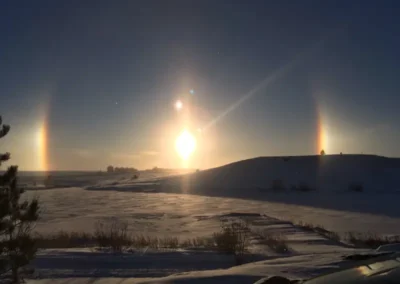 A stunning winter landscape with snow-covered ground, featuring brilliant sun dogs beside a bright sunrise on a clear blue sky